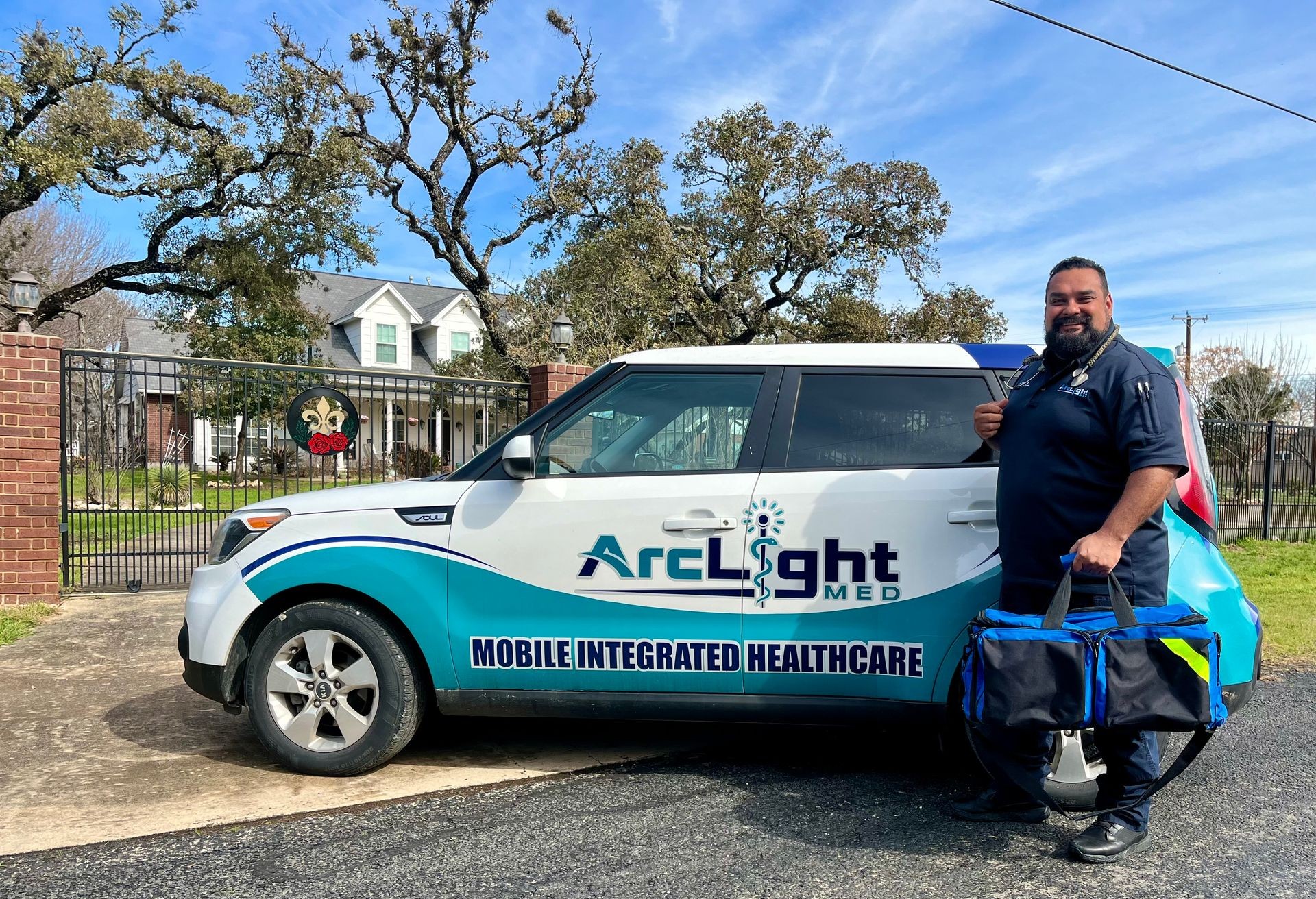 Man standing beside ArcLight Med vehicle with medical bag in front of a house and gate.