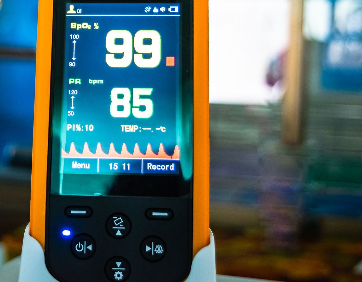 Close up Medical device, handheld pulse oximeter used to monitor patient blood oxygen  in the emergency room at the hospital, showing normal blood oxygen ninety-nine in yellow and pulse eighty-five. 